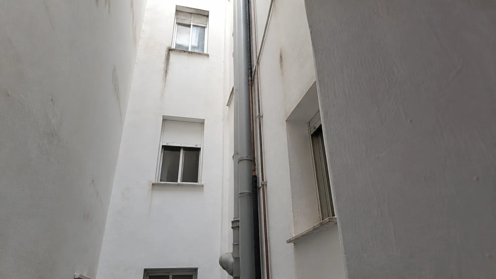 Bajante nueva de PVC gris con abrazaderas en el patio de luces de un bloque