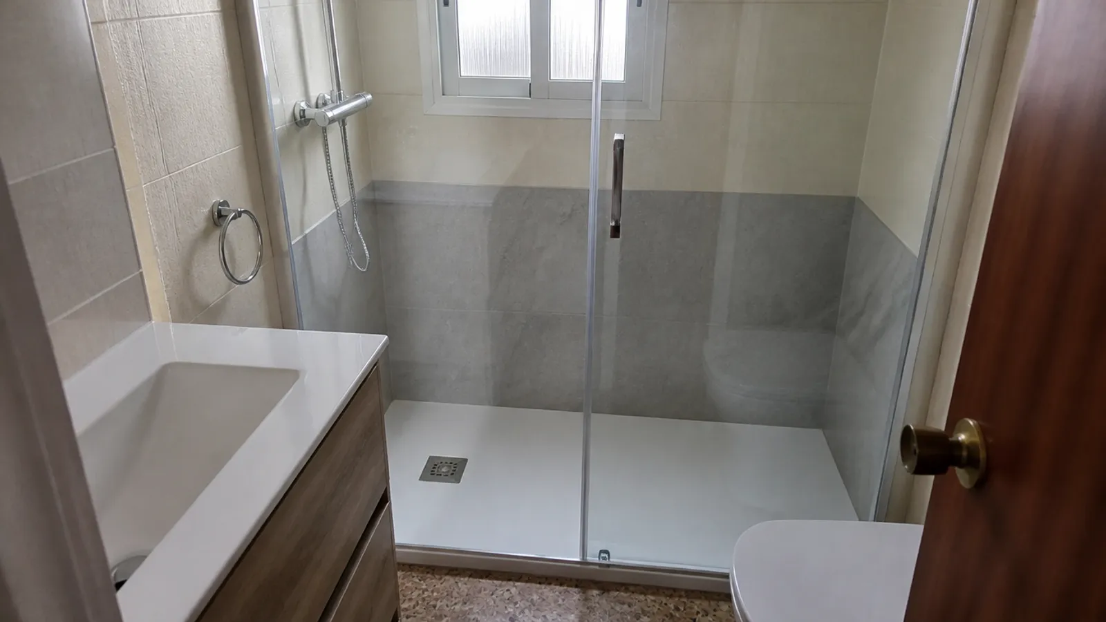 Plato de ducha extraplano blanco con mampara de vidrio en un baño pequeño reformado