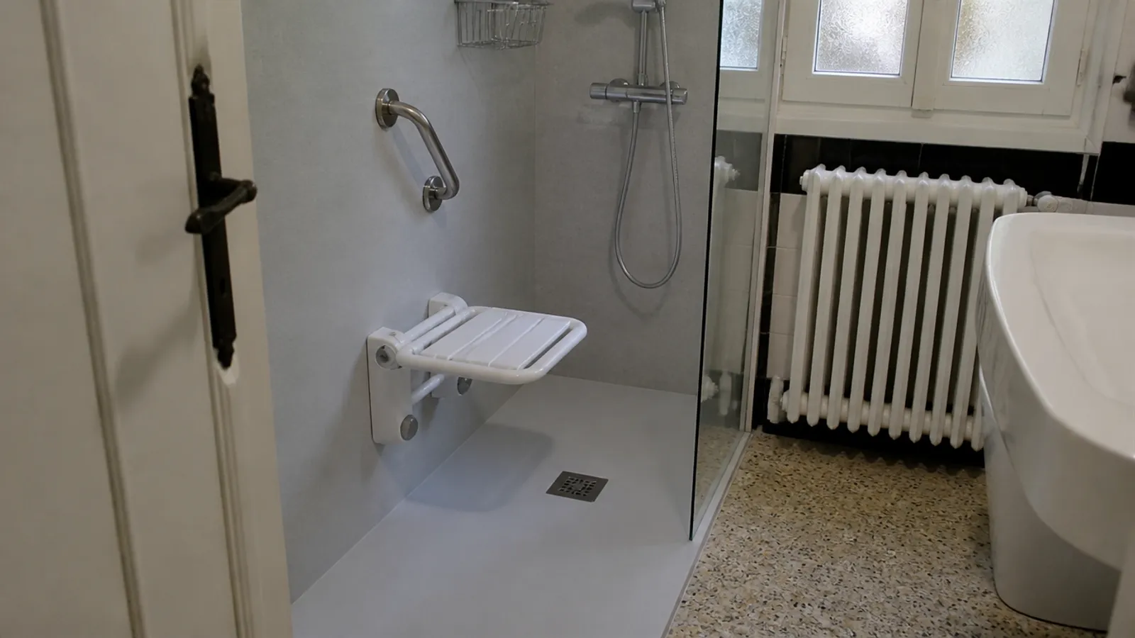 Ducha a ras de suelo con asiento abatible y asidero en un baño antiguo adaptado