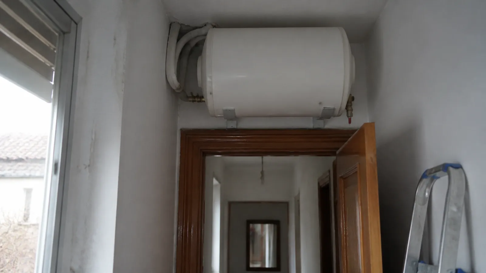 Termo eléctrico horizontal instalado sobre la puerta de un pasillo estrecho con soportes metálicos